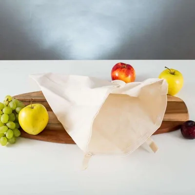 A white fabric bag is placed on a wooden cutting board with various fruits, including grapes, apples, and a plum.