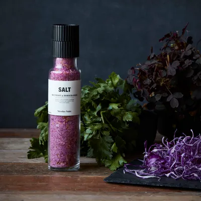 A bottle of pink salt with herbs and shredded red cabbage on a wooden table.