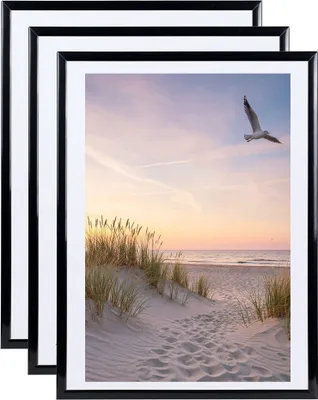 Three black picture frames are stacked on top of each other, with the front frame displaying a beach scene at sunset.