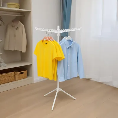 A white, foldable drying rack with clothes hanging on it, placed in a room with a closet and a window.