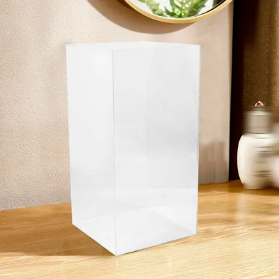 A clear acrylic display case on a wooden surface, with a blurred background showing a wall and a bottle.