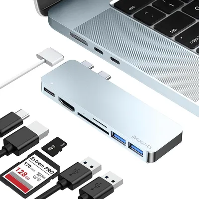 A silver USB-C hub is shown connected to a laptop, with various cables and memory cards arranged around it.