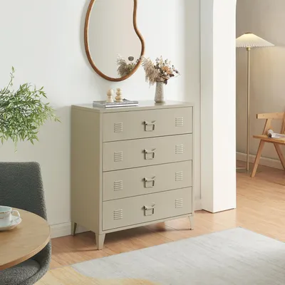 A camel-colored metal dresser with four drawers is placed in a room with a mirror, a plant, and a floor lamp.