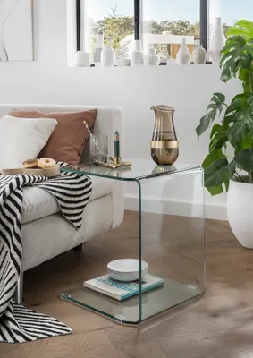 A glass side table next to a sofa, with a vase and books on it.