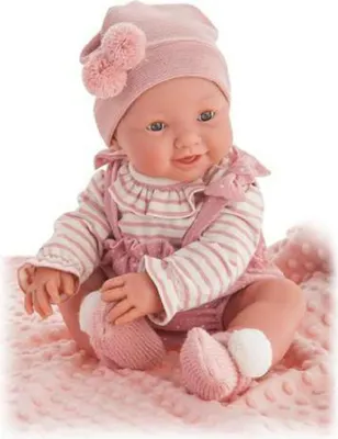 A baby doll dressed in pink clothing, sitting on a pink blanket.