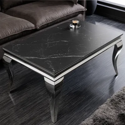 A black marble coffee table with chrome legs is placed in a living room setting next to a brown sofa.