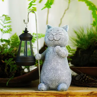 A garden statue of a cat holding a lantern, surrounded by plants.