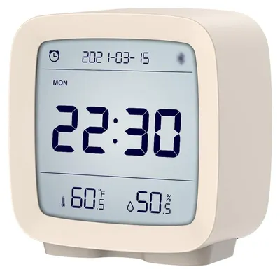 A digital alarm clock with a beige frame and a digital display showing the time, date, day of the week, temperature, and humidity.