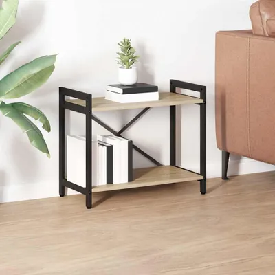 A two-tiered bookshelf with a wood-like finish and black metal frame, placed on a wooden floor next to a large green plant and a portion of a brown sofa.