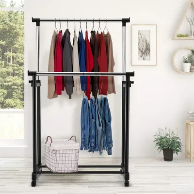 A double-tiered clothing rack with various clothes and jeans hanging on it, placed indoors near a window with greenery visible outside.