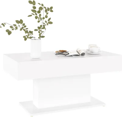 A white coffee table with a vase of green leaves, a magazine, and a cup of coffee on it.