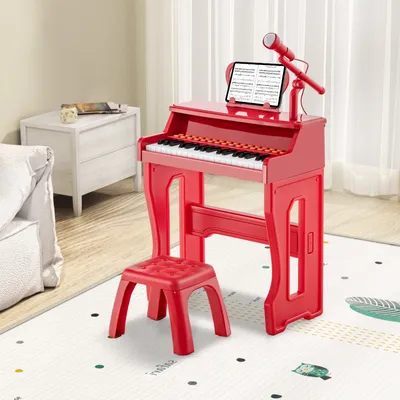 A red toy piano with a stool, microphone, and tablet stand is set up in a room with a white rug and a white dresser in the background.