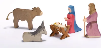 A nativity scene with wooden figures of Mary, Joseph, baby Jesus in a manger, a cow, and a donkey.