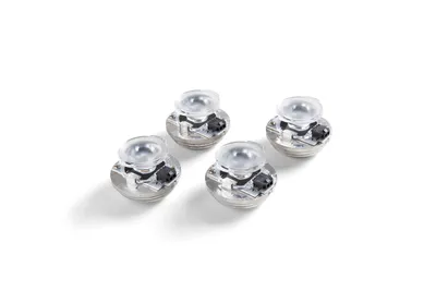 Four small, metallic-looking objects with clear plastic tops, arranged diagonally on a white background.