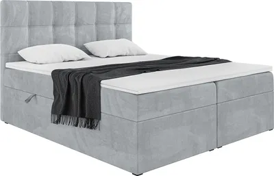 A light gray upholstered box spring bed with a headboard, two pillows, and a dark gray blanket.