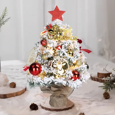 A small, decorated artificial Christmas tree on a table, surrounded by artificial snow and pinecones.