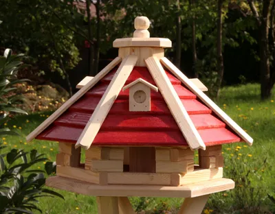 A wooden birdhouse with a red roof is set in a garden.