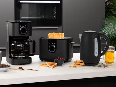 A black coffee maker, toaster, and electric kettle are displayed on a white countertop in a modern kitchen setting.