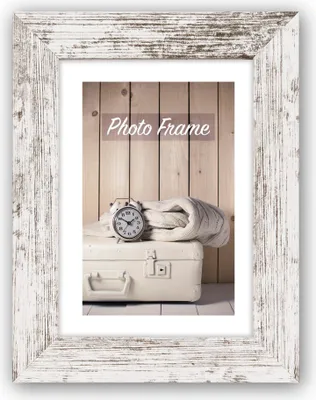 A vintage-style alarm clock and a folded blanket rest on a cream-colored suitcase, set against a backdrop of vertical wooden planks. The scene is framed by a distressed white wooden picture frame.