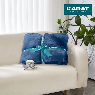 A folded dark blue blanket is placed on a cream-colored sofa, with a cup and saucer to its left. A plant is visible in the background.
