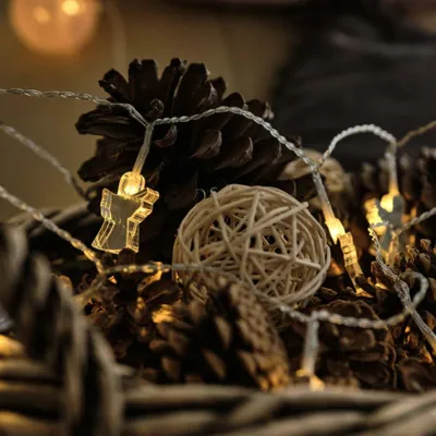 A close-up view of a string of fairy lights with angel-shaped LEDs intertwined with pinecones and a woven ball.