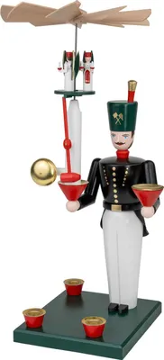 Das Bild zeigt eine traditionelle Holzfigur eines Bergmanns in schwarzer Uniform mit grüner Mütze der auf einem grünen Sockel steht und eine Pyramide mit Flügeln über seinem Kopf hält während er in der Hand einen roten Kerzenhalter trägt