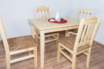 A wooden dining table with four chairs in a room with white walls and wooden flooring.