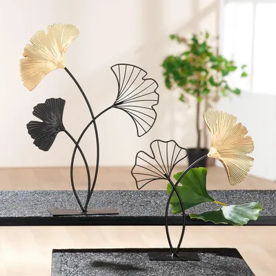 Two decorative ginkgo leaf sculptures on a textured surface, with a blurred plant in the background.