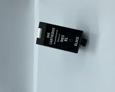 A black ink cartridge is placed on a light gray and white surface.