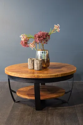 A round wooden coffee table with a metal frame and a lower shelf, decorated with a vase of flowers and two wooden candle holders.