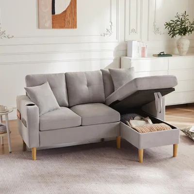 A light gray sectional sofa with its storage ottoman open, revealing stored items. The sofa is in a well-lit living room with decorative elements on the wall and a dresser in the background.