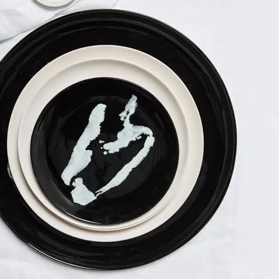 A stack of three plates, with the top plate featuring a black base and white abstract design.