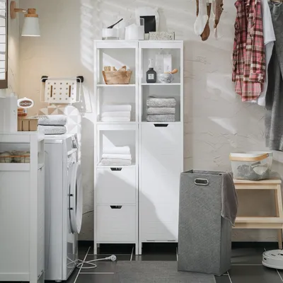 A laundry room scene with a white storage unit, washing machine, laundry basket, and hanging clothes.