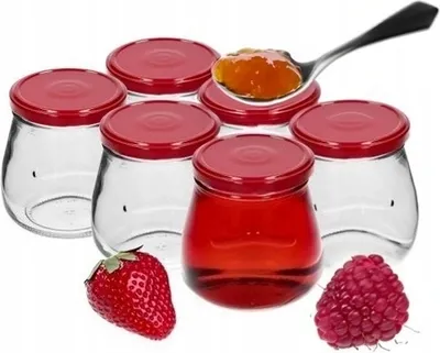 A group of empty glass jars with red lids, a spoon with jam, a strawberry, and a raspberry.