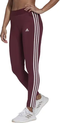 A woman wearing burgundy Adidas leggings with white stripes and white sneakers, shown from the side.