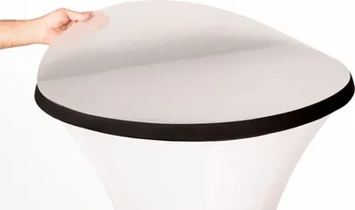 A hand is shown holding the edge of a white circular tabletop with a black trim, which is placed on top of a white stand or base.