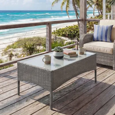 A coffee table on a wooden deck overlooking a beach and ocean.