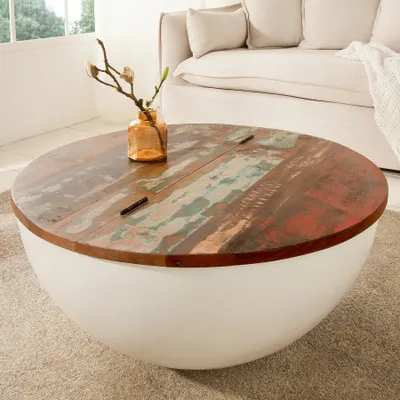 A round coffee table with a reclaimed wood top and a white bowl-shaped base, placed on a rug in a living room setting.
