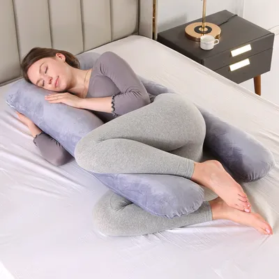 A woman is sleeping on a bed, using a U-shaped pregnancy pillow.