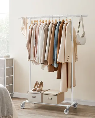 A white clothing rack filled with various garments, including jackets, shirts, and dresses, all in neutral tones. Two beige storage boxes and a pair of beige high-heeled shoes are placed on the bottom shelf. A white handbag with a chain strap is hanging fr
