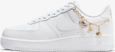A side view of a white Nike Air Force 1 '07 LX sneaker with gold charms attached to the laces.