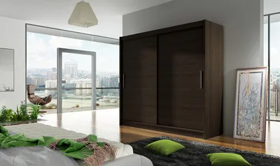A bedroom with a large sliding door wardrobe, a bed with green blankets, and a large window overlooking a city.