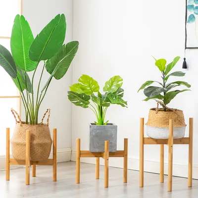 Three artificial plants in pots are displayed on wooden plant stands against a white background.