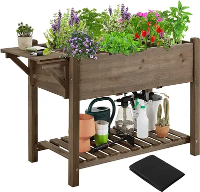 A wooden raised garden bed filled with various plants, herbs, and flowers, with gardening tools and accessories stored underneath.