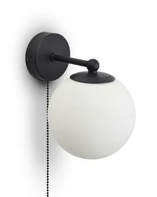 A black wall lamp with a white glass globe shade and a pull chain, mounted on a white wall.