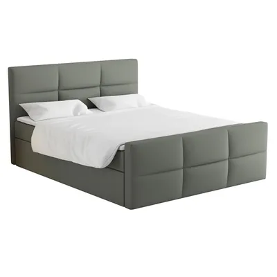A studio shot of a gray upholstered boxspring bed with white bedding and pillows.