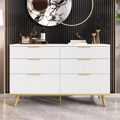 A white dresser with gold accents and legs, set against a black paneled wall with a decorative mirror above it.