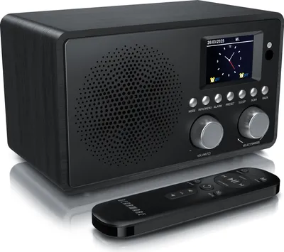 A black DAB+ radio with a display screen and two control knobs, shown with a remote control in front of it, all on a white background.