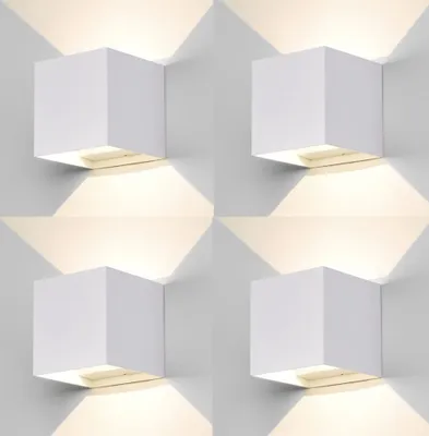 Four white cube-shaped wall lights are mounted on a white wall, casting warm light downwards and upwards.