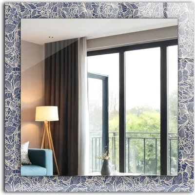 A mirror with a floral pattern frame reflecting a room with a lamp, a chair, and a window overlooking greenery.